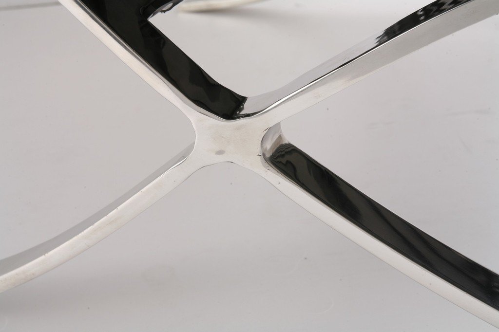 : Polished steel X-frame of a red Barcelona chair, mirror finish with riveted leather straps.