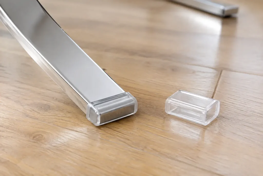 Clear feet protector sleeve fitted to the flat steel foot of a Barcelona chair on an oak floor